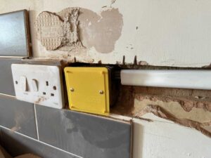 Exposed wall with electrical fittings visible.